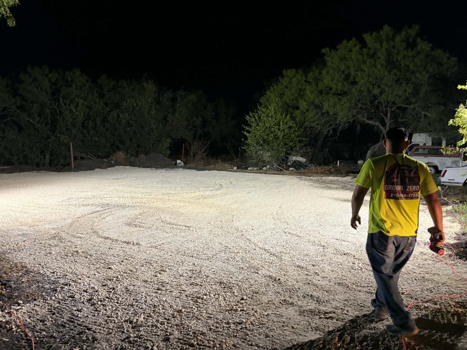 Ground Zero crew member walking a freshly graded gravel pad at night